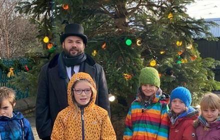 A staff member in a black top hat, posing for a photo with five children.