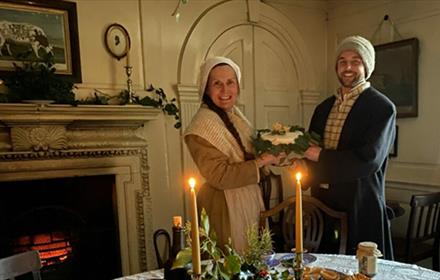 Two members of staff in Georgian clothing, holding Christmas cake.