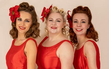 The Darling Dollies posing for a photo in red vintage dresses with vintage hair and makeup.