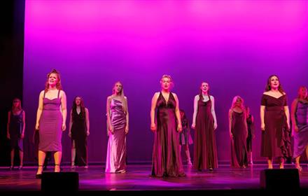 Performing Arts students of New College Durham's Class of 2025 on stage in long dresses.