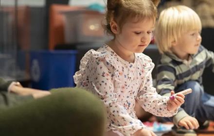 Child holding a crayon, sitting with other children at Little Dragons.