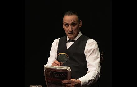 Sherlock Holmes reading a newspaper through a magnifying glass