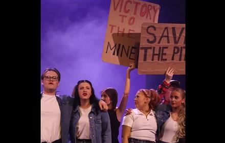 A group of young people holding up signs saying, 'SAVE THE PITS' and VICTORY TO THE MINERS'
