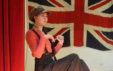 Actor in a cap in front of a Union Jack flag. Beamish Museum Pantomime 2026.