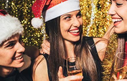 3 women in Santa hats laughing and drinking from champagne flutes.