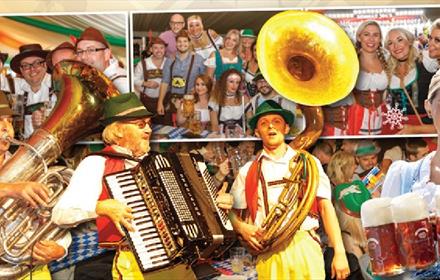 Poster showing 'The Amazing Bavarian Stompers Show'. Musicians, a Bavarian woman with beer and people smiling.