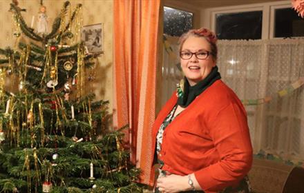 A woman stands next to a Christmas tree with traditional decorations