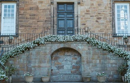 Lumley Castle exterior. Two staircases, bordered by shrubs, lead to a door.