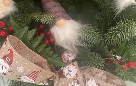 Festive greenery, decorated with a gonk and festive ribbon which has a pattern of snow flakes and gonks on it.