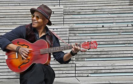 Guy Davis wearing a hat and holding a guitar