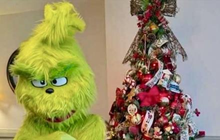 The Grinch in front of a Christmas tree.