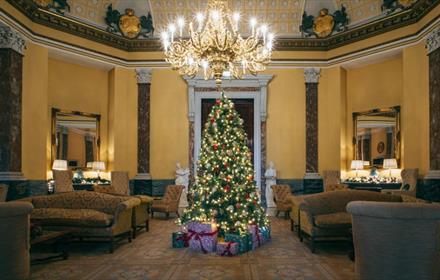 Christmas tree with presents under an opulent candelabra in a comfortable lounge area.