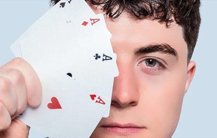 Close up of Tom Bolton holding a suit of aces which cover one side of his face.