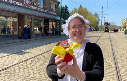 A member of staff in traditional clothing holding an Easter Egg with a yellow bow on it