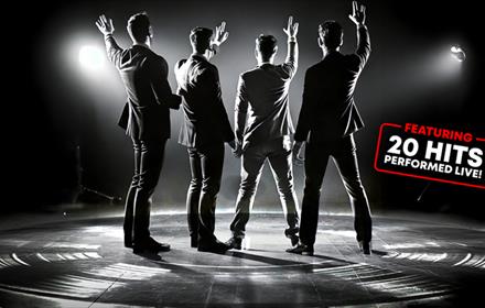 Black and white photo of a 'Frankie Valli and the Four Seasons' tribute band on stage, waving at the crowd.