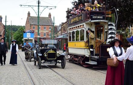 Staff in character at Beamish Museum, next to vintage cars and a tram - 1900s Town