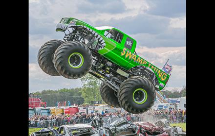 Crowds watching Monster Trucks crushing a row of cars