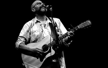 Black and white image of Steve Pledger playing guitar and singing on stage