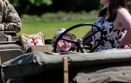 Small child sitting at the wheel of an army truck.