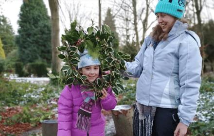 A young girl holding a Christmas Wreath, standing beside a woman outdoors.