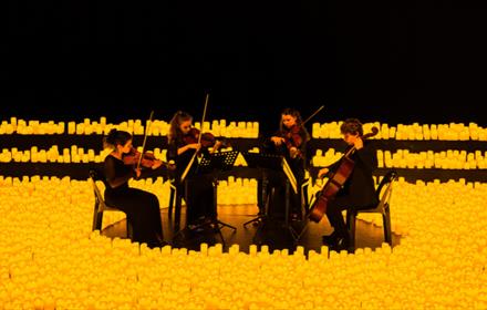 Group of musicians playing string instruments surrounded by hundreds of candles.