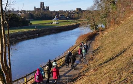 A group walking along the River Wear, with stunning views of the bandstand and Durham Cathedral and Castle.