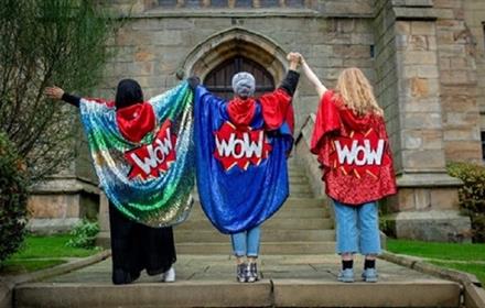WOW Women of the World Festival Three women wearing colourful cloaks with WOW logo on the back