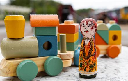Train and carriage made from colourful wooden blocks with a painted peg doll