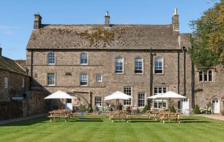 View of the Lord Crewe Arms on a bright sunny day with people sat in the garden under white umbrellas.