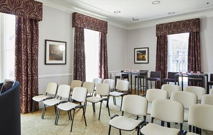 Neville room set up theatre style with white chairs
Light coloured walls with dark red, patterned curtains on 3 windows