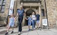 Image of different generations of a family smiling and holding hands as they leave Palace Green Library.