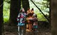 Two children standing beside wooden sculpture.