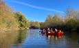 Groups of people paddling red canoes down a calm river surrounded by autumn trees under a clear blue sky.