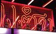 A neon sign of Thai letters, accompanied by a line of Lucky cats - the sign spells out 'ZAAP' written in Thai