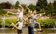 Four children laughing and jumping in the air in front of a pond at Durham University Botanic Garden.
