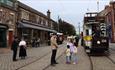 A family talking to staff in character in front of a tram at Beamish 1900s Town