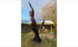 Two tree carvings with a stone wall behind and fields in the distance.