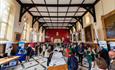 A busy exhibition and networking hall 
(The Refectory) filled with display tables and attendees