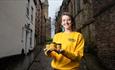 Owner of Durham mustard, Anya Kirkby, wearing a yellow Durham mustard jumper whilst holding 3 jars of mustard