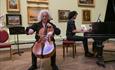 A man playing a cello and a man playing the piano room in the picture gallery.