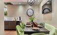 A different view of the kitchen from the dining table.
Black table with green chairs around it. TV is on the wall above the dining table