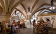 Two families sit at tables in a cafe, which has an arched stone roof.