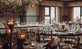 The Orangery, with friendly folk pelmets, soft grey ticking curtains, lime-washed furniture, and clothed tables with floral centrepieces and candles.