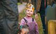 Little girl in purple jumper and trousers smiling at camera wearing Gruffalo birthday paper crown.