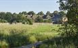 A view of Headlam Hall taken from an area of the golf course surrounded by some bushes and trees. A small foot bridge goes through the bushes.