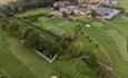 An aerial view of Headlam Hall and part of the golf course. Sand bunkers and greens can be seen from above along with a tennis court and gardens.