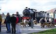 Visitors sat on picnic benches. Behind the benches is a locomotive that visitors are viewing.