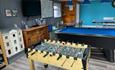 A games room with a snooker table, foosball table, ping pong table, wooden dolls house and television on the wall.