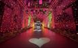 Playing cards suspended from beams in an illuminated, colourful tunnel with heart shapes on the floor.