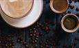 Image shows coffee cups on a table covered in coffee beans.